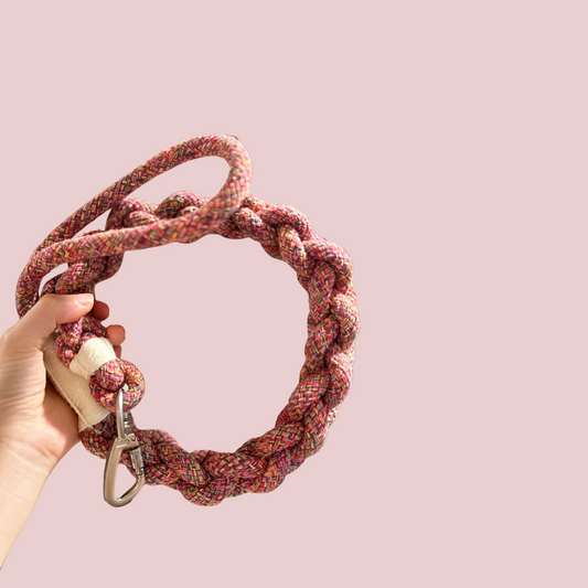 Red Rope dog Leash with a carabiner held by a hand against a pink background