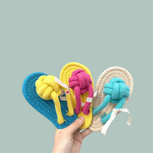 Three colorful knotted slipper rope toys held by a hand against a light gray background