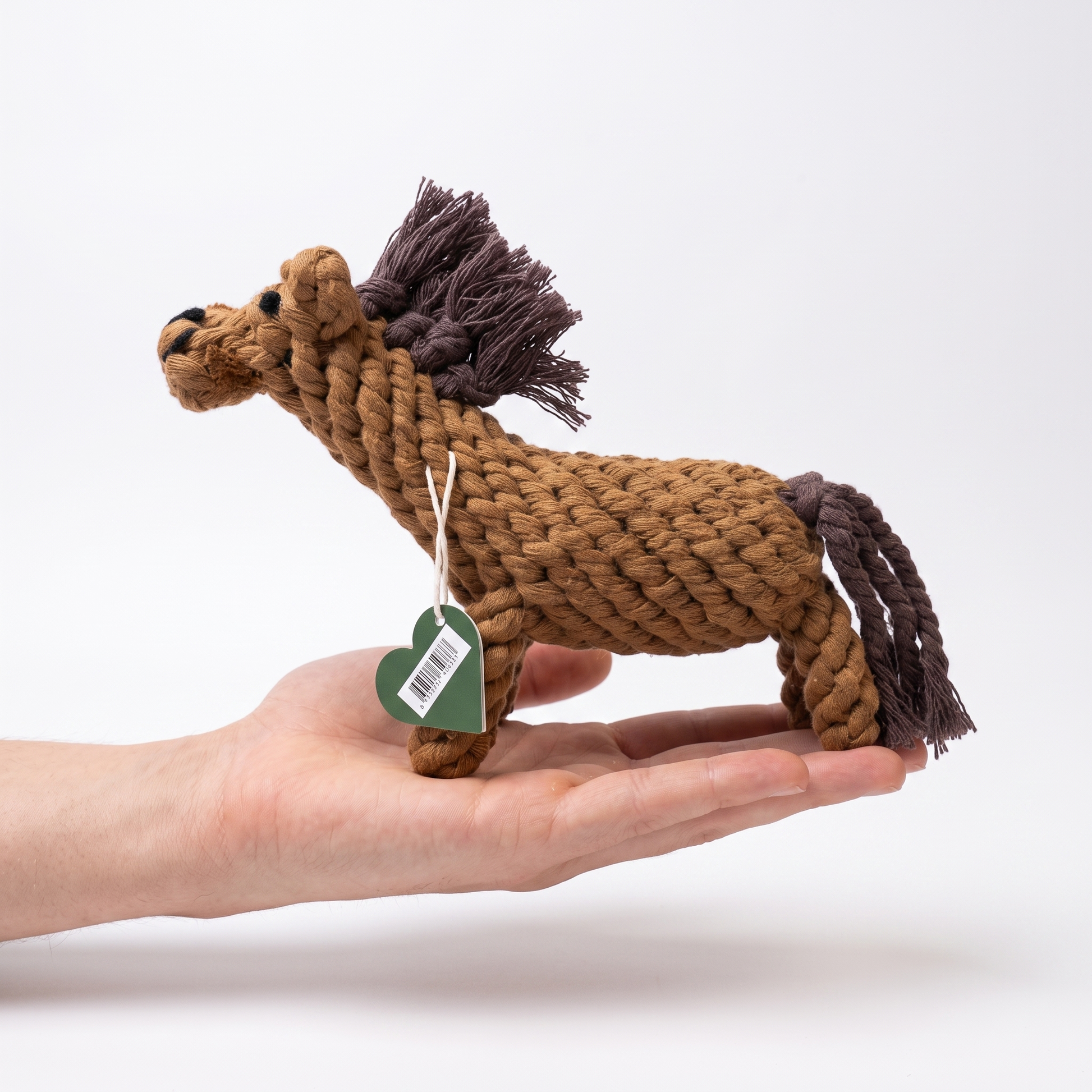 A small rope horse dog toy in brown and dark brown, held in a person's hand against a clean white background.