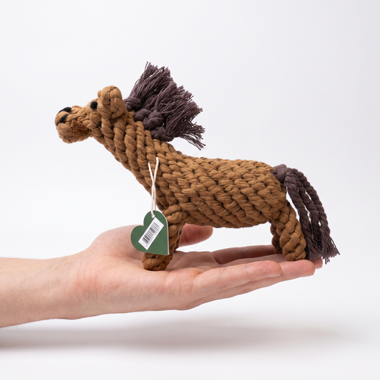 A small rope horse dog toy in brown and dark brown, held in a person's hand against a clean white background.