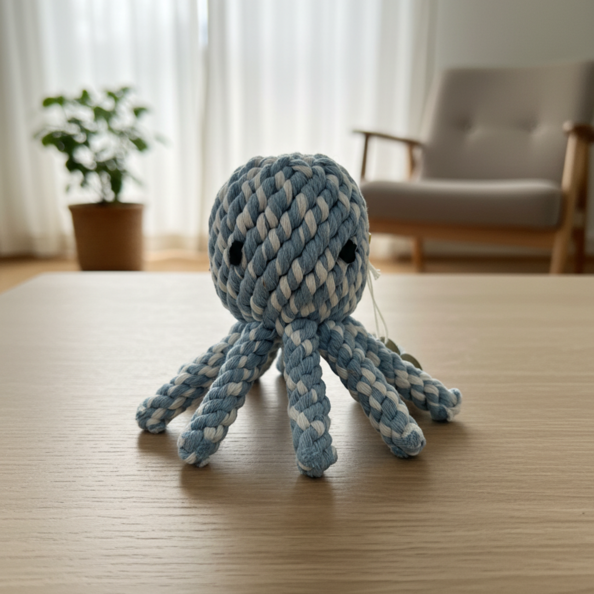 Blue and white braided octopus toy on a wooden table with a blurred indoor background