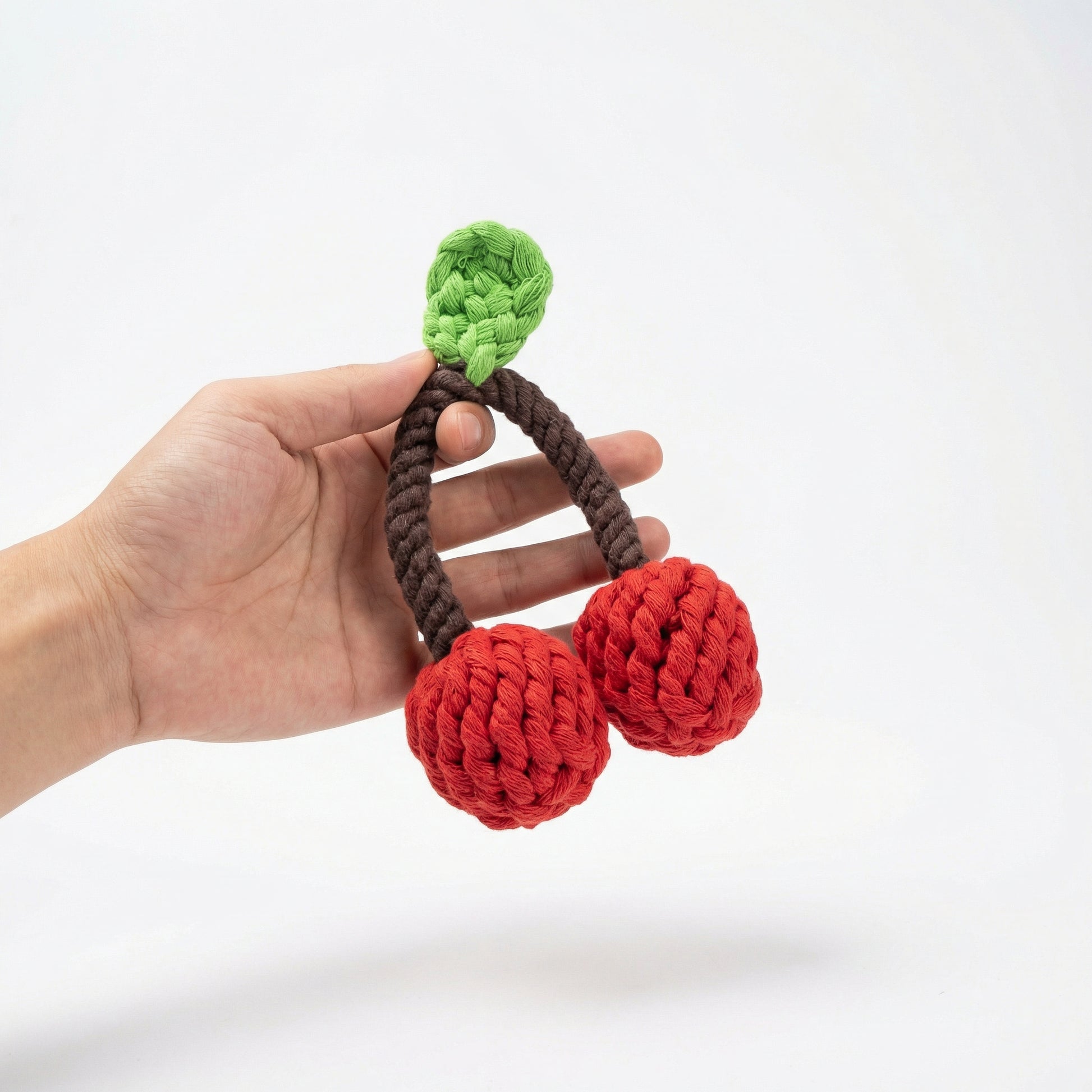 Hand holding a crocheted cherry toy with a white background