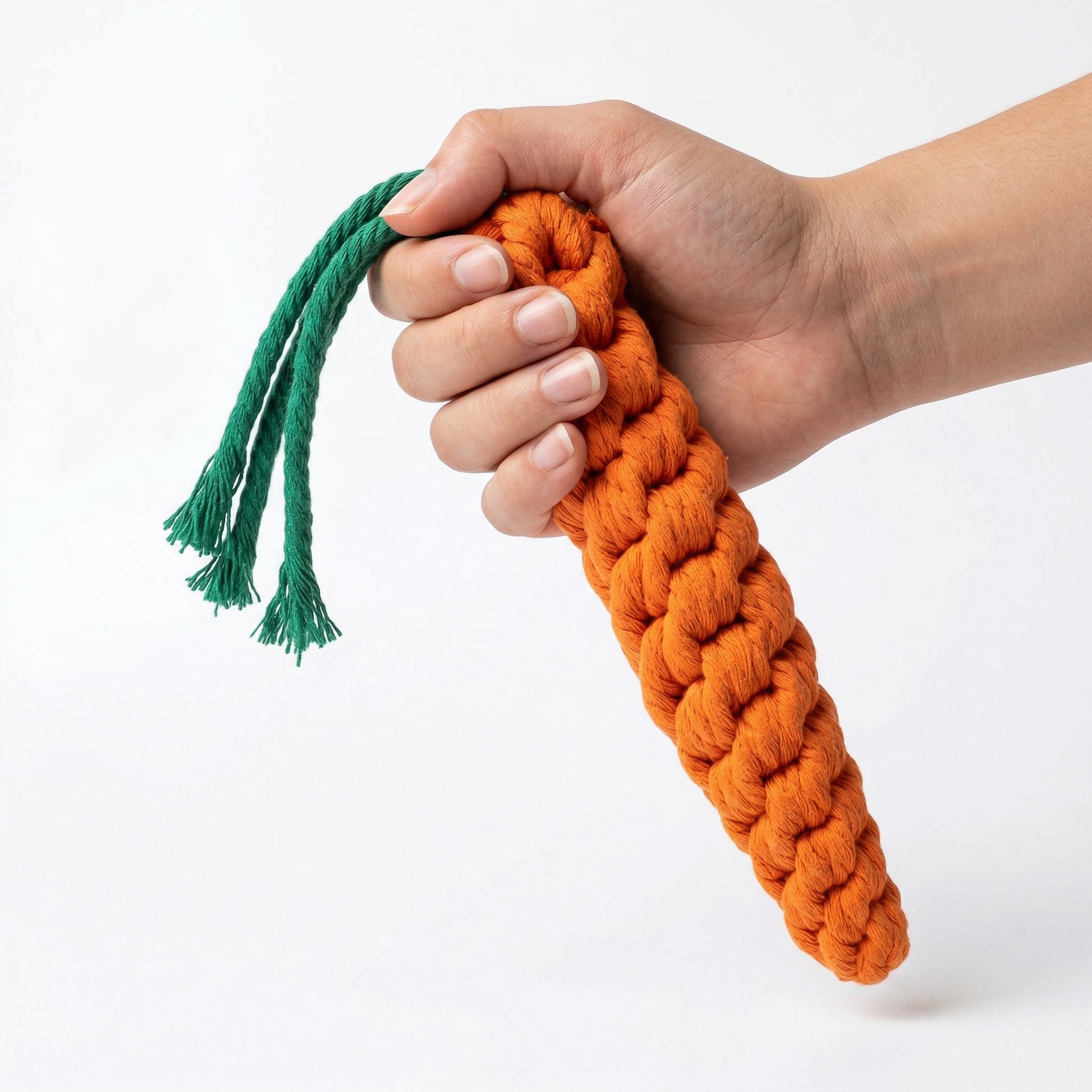 Hand holding a braided orange carrot toy with green top on a white background