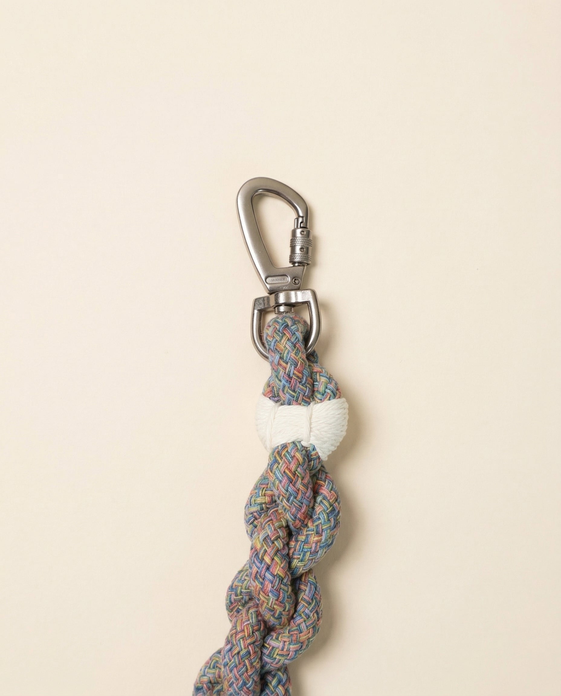 Multicolored braided rope keychain with a metal carabiner on a beige background