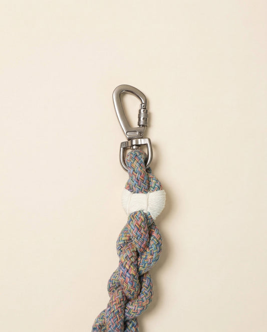 Multicolored braided rope keychain with a metal carabiner on a beige background