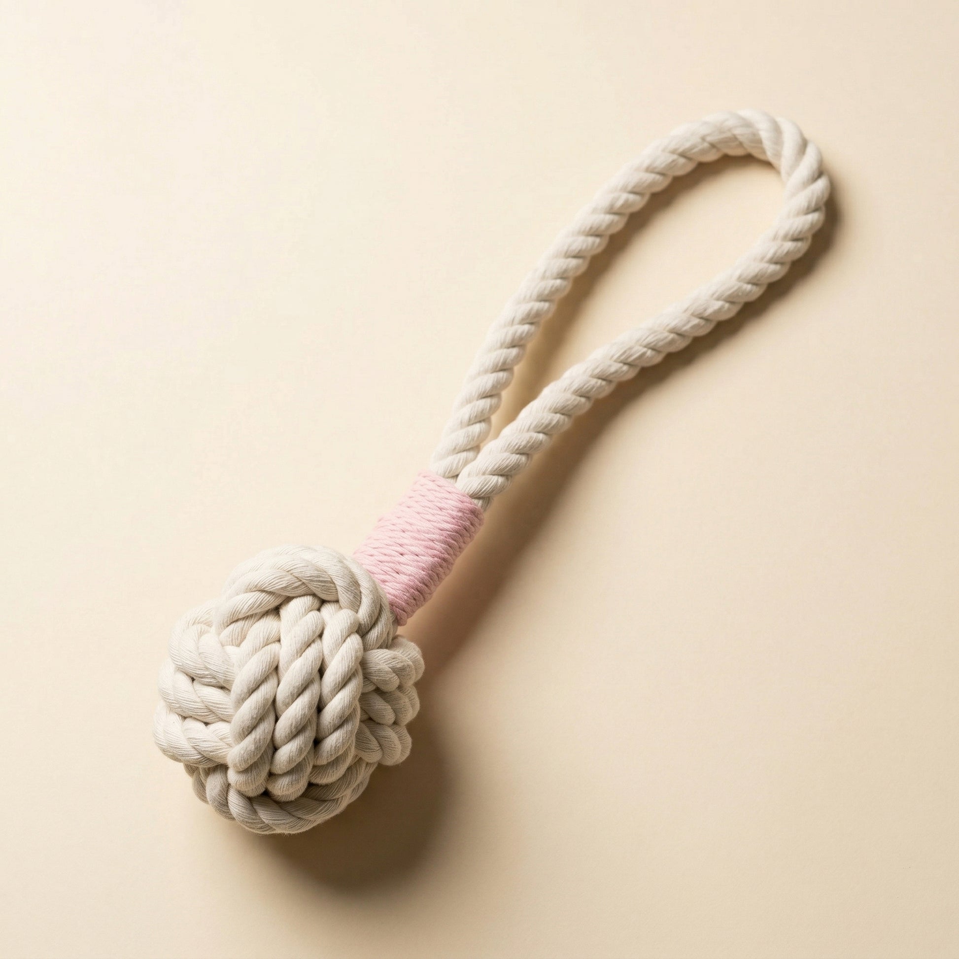 Dog toy with a knotted rope ball and pink center on a beige background