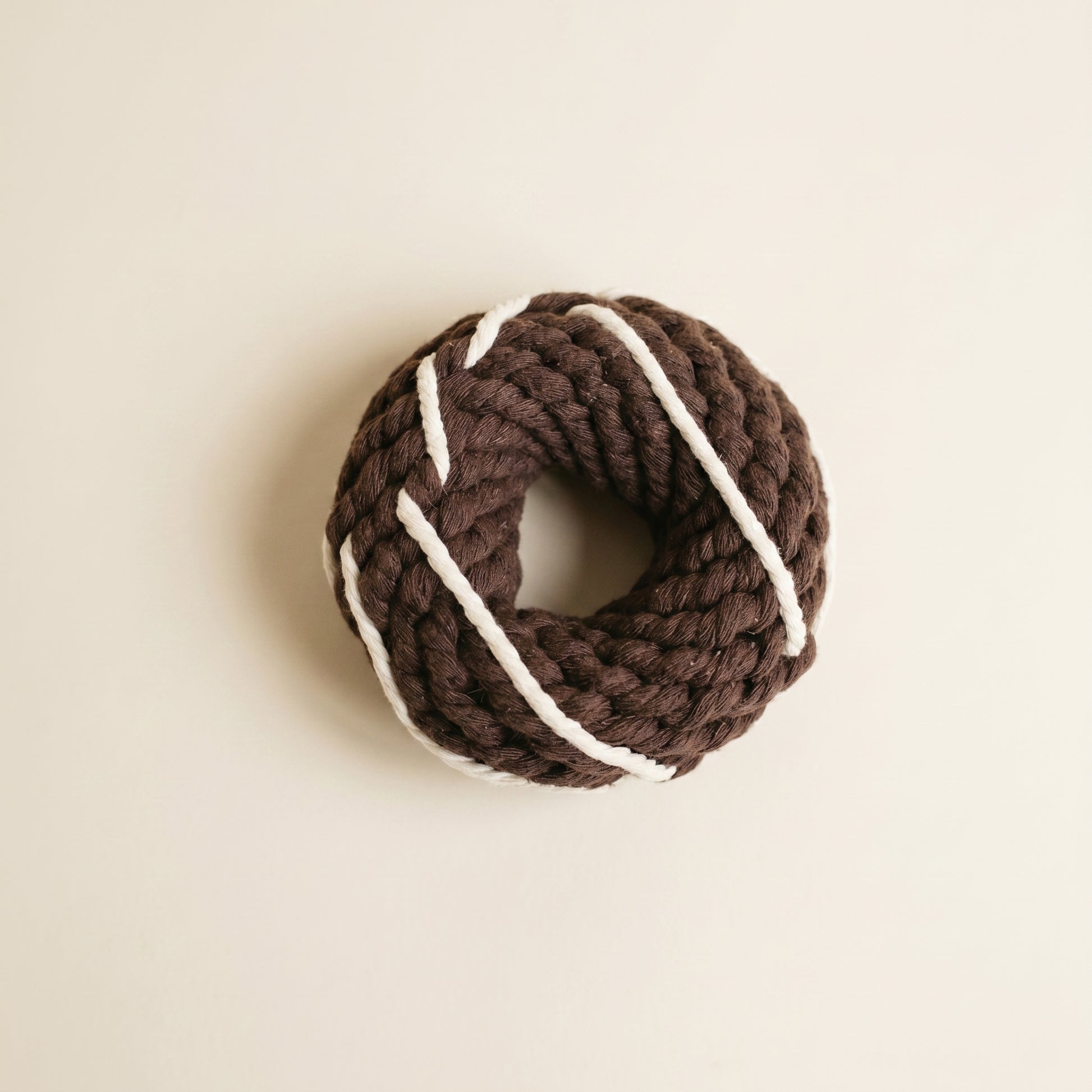 Brown knitted dog donut toy with white stripes on a beige background