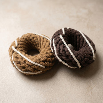 Two knitted donut toys, one brown and one dark brown, on a beige surface.