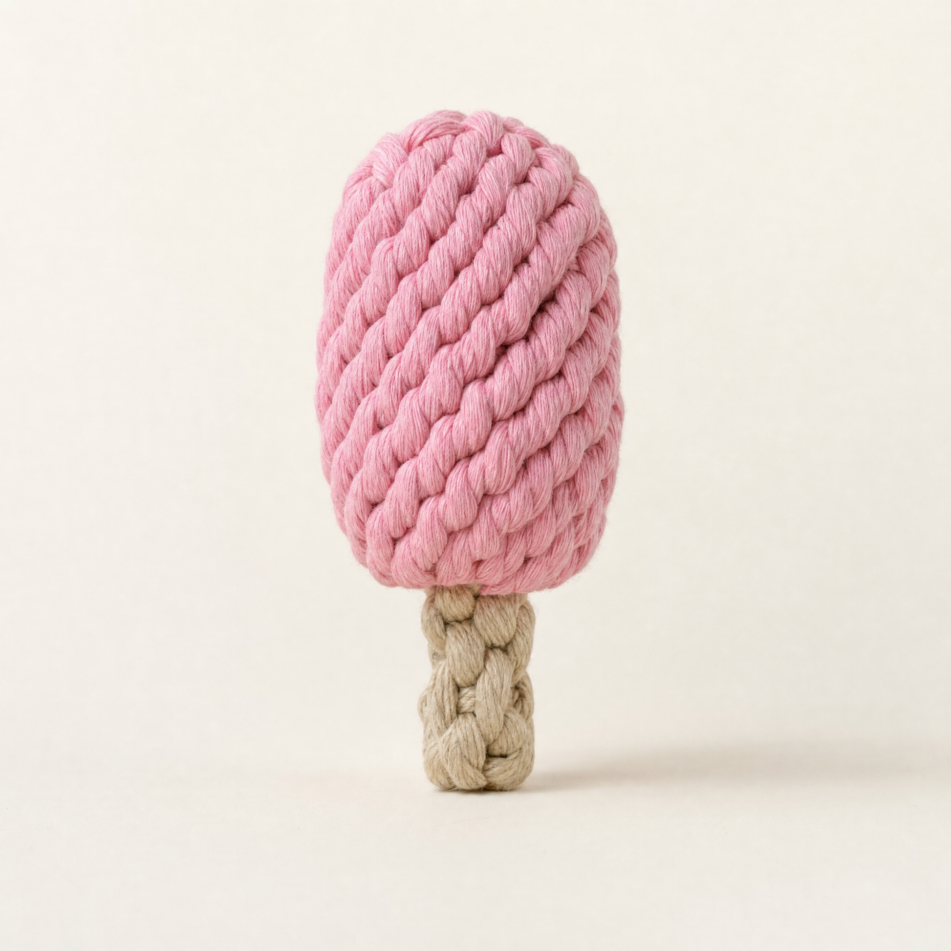 A pink and beige rope dog toy shaped like a popsicle, featuring a thick textured pink top and a knotted beige handle, photographed on a clean off-white background.