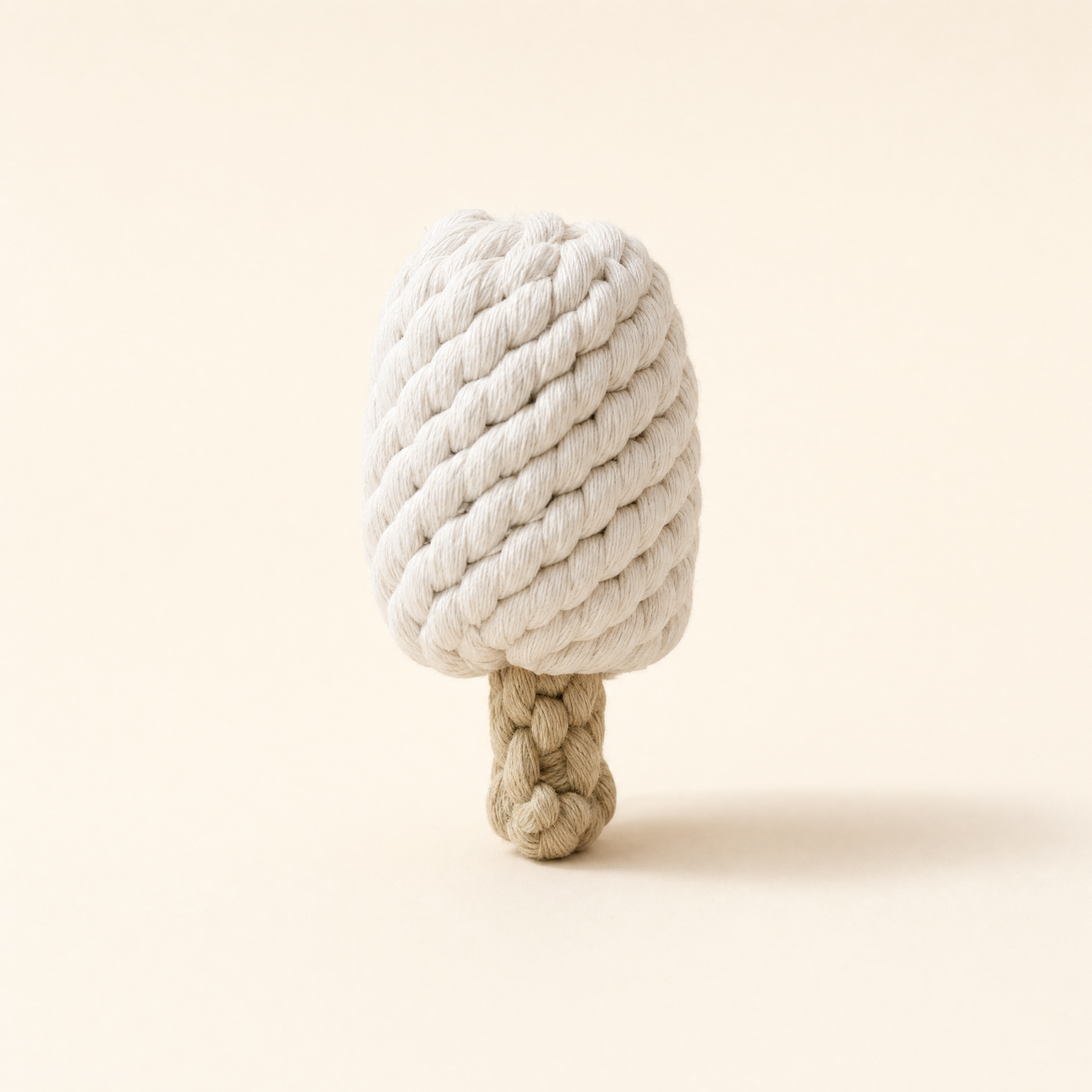 A ice cream bar dog toy made of thick, textured rope, featuring a cream-colored top and a natural tan base, set against a solid cream background.