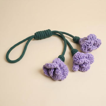 A handmade daylily snuffle dog rope toy featuring three knotted purple crochet flowers attached to a dark green rope loop, displayed on a light beige background.