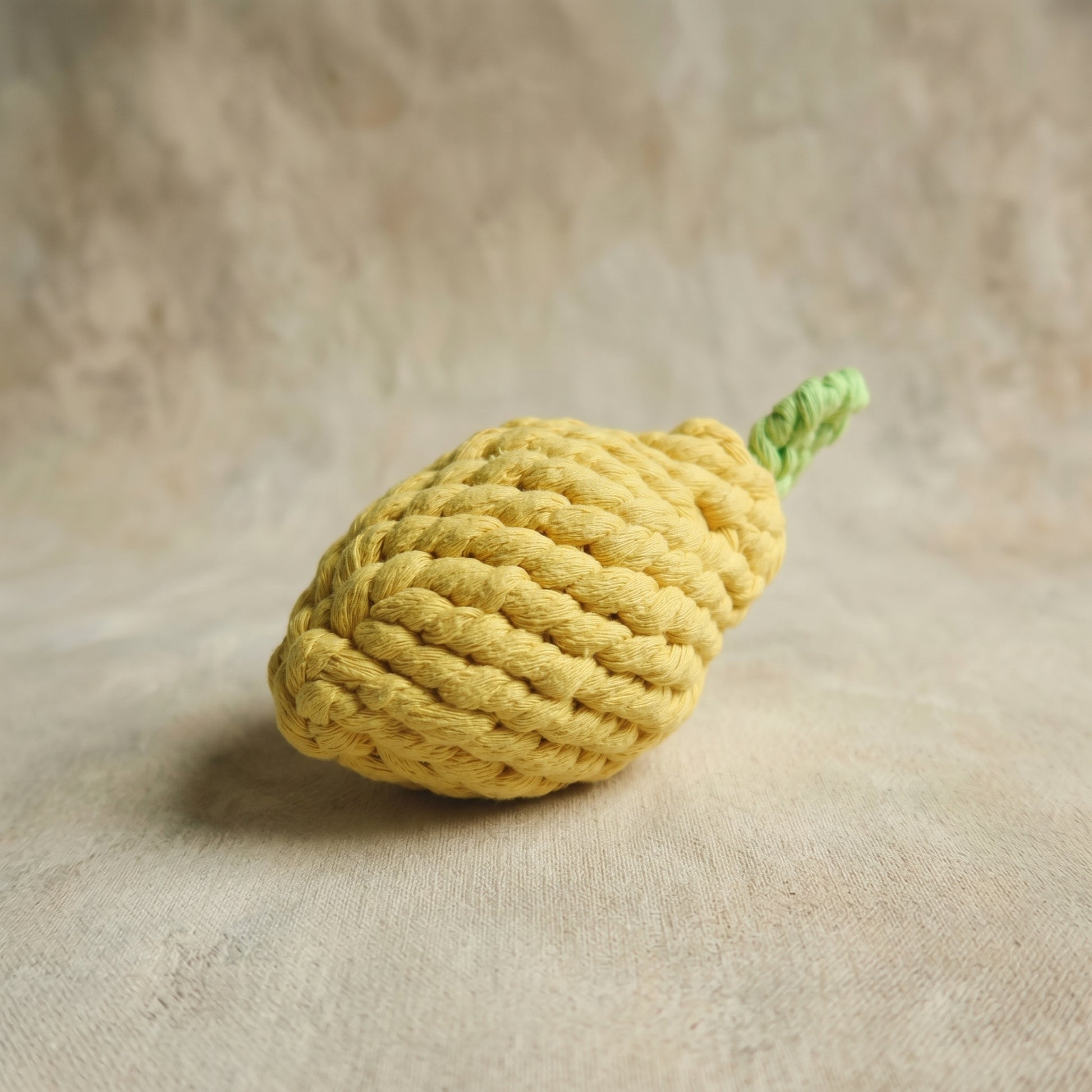 Yellow knitted lemon-shaped toy on a beige surface